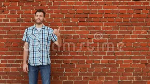 穿着衬衫和牛仔裤的时髦留胡子的人指出要复制空间砖墙背景视频的预览图