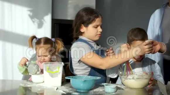 厨房里的孩子大一点的女孩把鸡蛋打碎到面团里然后从碗里过去妈妈和女孩视频的预览图