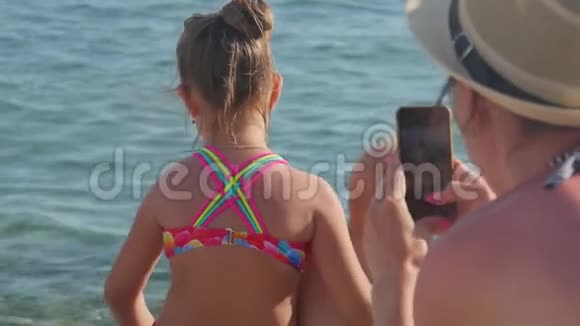 快乐的母亲在户外海滩上用智能手机给她的孩子拍照妈妈给家人拍照视频的预览图