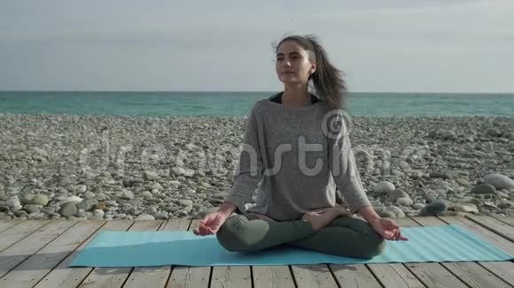 女人在海边平静地放松做瑜伽体式坐在地板上视频的预览图