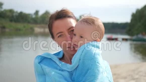 妈妈和小男孩在海滩上的毛巾上可爱的小男孩洗澡后被裹在毛巾里视频的预览图