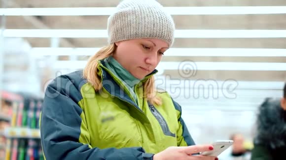 超市里的一位女士手里拿着一部智能手机她正靠在一个装满货物的篮子上等着排队视频的预览图