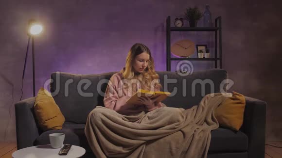 一个年轻的女人坐在沙发上看书女孩在温暖的房间里的舒适沙发上做梦视频的预览图