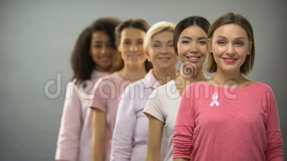 微笑着穿着粉红色衬衫戴着乳腺癌丝带的女人站在一边支撑着视频的预览图