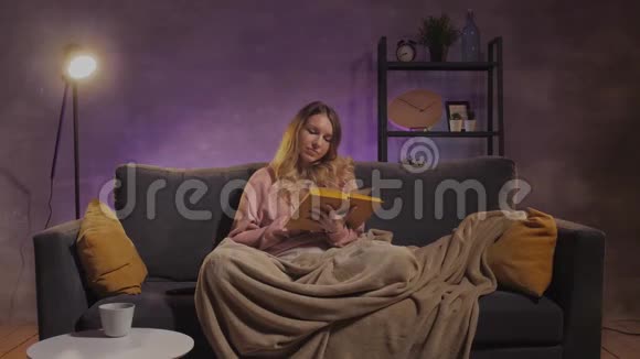 一个年轻的女人坐在沙发上看书女孩在温暖的房间里的舒适沙发上做梦视频的预览图