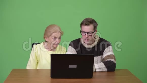 高级女商人和年轻男子一起使用笔记本电脑视频的预览图