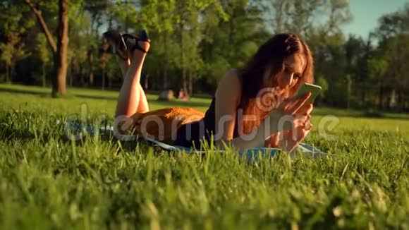 快乐女类型短信或聊天坐在公园的草地上女人在电话里聊天视频的预览图
