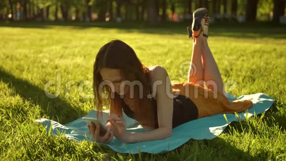 漂亮的女士一边打电话一边躺在草地上视频的预览图