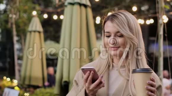 时尚年轻可爱的微笑女孩在城市散步时使用现代智能手机的肖像女士打字短信视频的预览图