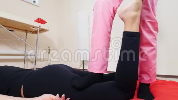 年轻女子躺在垫子上接受按摩伸展腿部肌肉视频的预览图