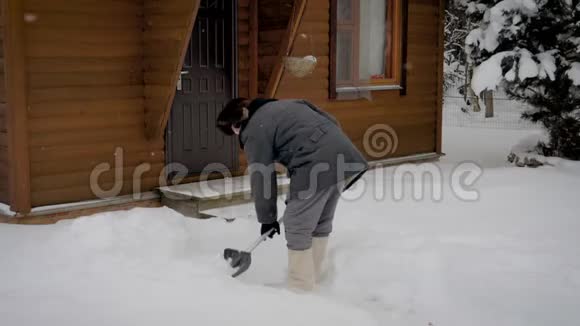 冬天木屋的背景下人们从白雪中清理一个铲场视频的预览图