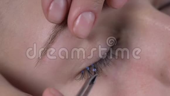 化妆师用镊子将塑料睫毛延长部分粘在顾客的眼睛上视频的预览图