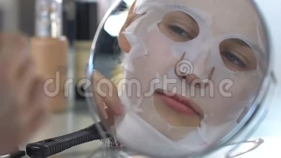 美丽的女孩在前镜下摘下保湿组织面膜完美的皮肤视频的预览图