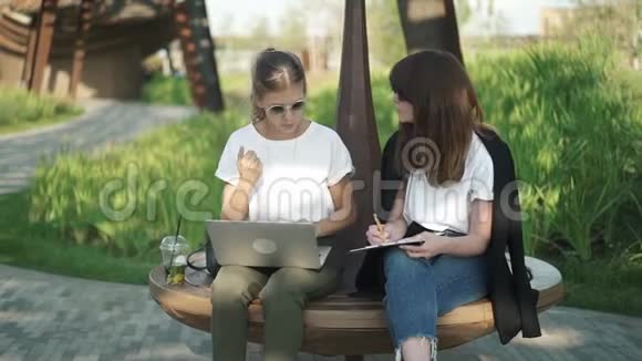 两个漂亮聪明的女人用笔记本电脑工作或者在夏季公园学习视频的预览图