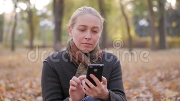 坐在黄色叶子上的女人使用智能手机应用程序短信或看照片视频的预览图