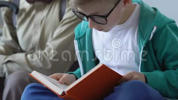 聪明的男孩有兴趣看书爷爷坐在沙发上听着视频的预览图