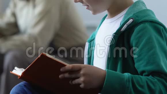 男孩拿着书和父亲坐在沙发上看书和导师一起上课视频的预览图