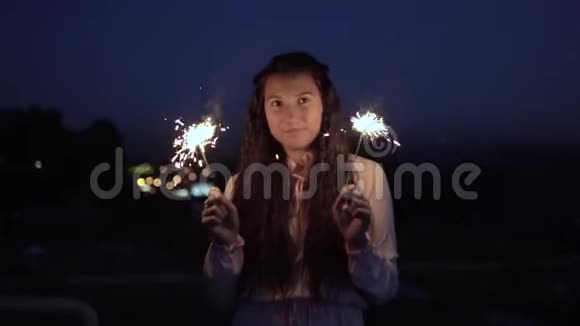 一个穿着裙子的年轻女孩站在一个夜晚城市的背景下手里拿着烟花慢动作视频的预览图