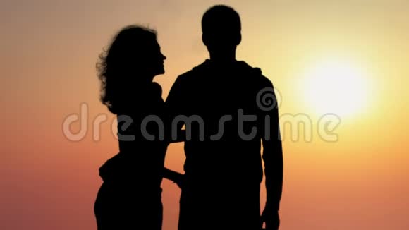 年轻女子亲吻男友欣赏美丽日落的剪影视频的预览图