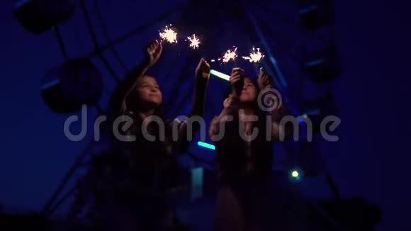 两个女孩手里拿着烟花在摩天轮的背景上慢动作视频的预览图