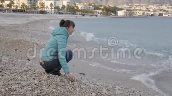 孤独寒冷海滩的女人白种人女人从迎面而来的海浪中跳出来在水面上玩石头视频的预览图