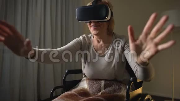 坐在轮椅上享受现代虚拟现实耳机乐趣的兴奋的高级女士视频的预览图