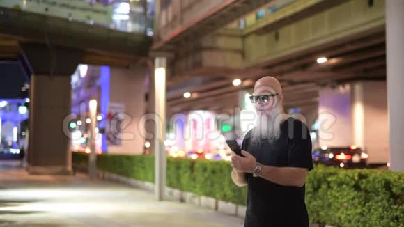 成熟的秃头游客晚上在城里用电话视频的预览图