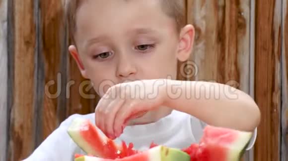 孩子坐在木墙背景的桌子旁吃西瓜视频的预览图