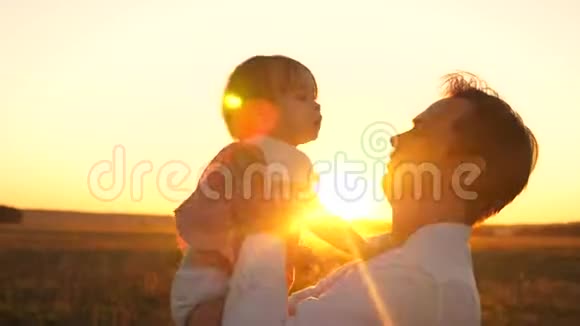 快乐的爸爸在公园的金色太阳日落时和宝宝玩婴儿在教皇手中微笑日落特写视频的预览图