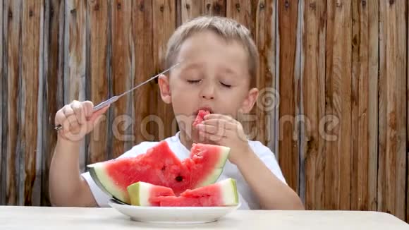 孩子坐在木墙背景的桌子旁用刀吃西瓜视频的预览图