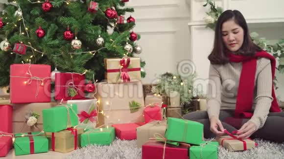 快乐的年轻亚洲女人在圣诞节的时候包装圣诞礼物装饰她家的客厅视频的预览图