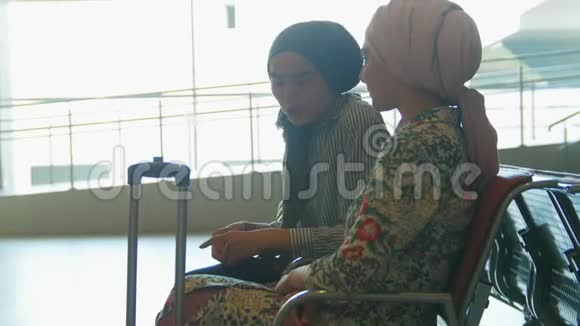 两个微笑的穆斯林妇女在机场的客厅里互相交谈a视频的预览图