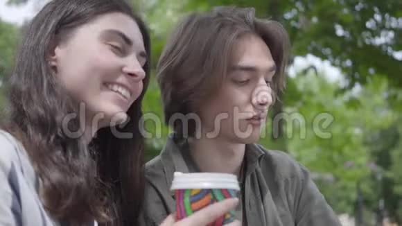 描绘了一对年轻幸福的夫妇穿着休闲服装在公园里聚在一起约会学生们喝酒视频的预览图