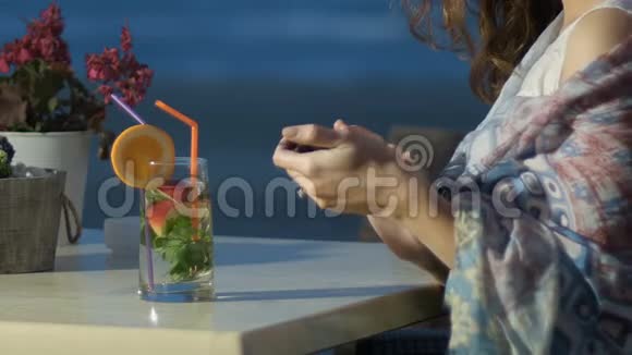 浪漫的女人在智能手机上输入信息喝新鲜鸡尾酒放松视频的预览图