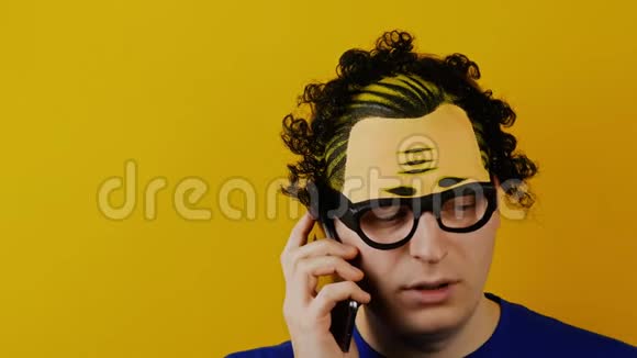 卷毛的家伙在智能手机上认真地说话黄色的墙背景黑色的头发视频的预览图