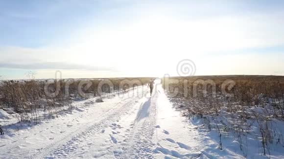 一个年轻的女孩欢快地走着跳上一片白雪覆盖的田野冬天阳光明媚的欢乐景象有一条路和一片雪域视频的预览图