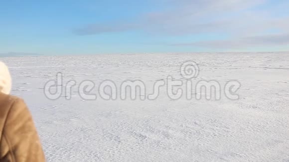 一个年轻的女孩欢快地走着跳上一片白雪覆盖的田野冬天阳光明媚的欢乐景象有一条路和一片雪域视频的预览图