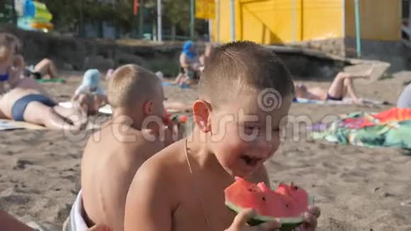 孩子们在海滩上玩沙子里的男孩吃西瓜这孩子手里拿着一块绿色的瓜皮头视频的预览图
