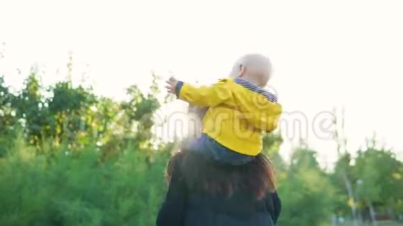 日落时分妈妈和她的孩子在公园里玩男孩穿着一件黄色夹克坐在他的肩膀上开心地笑着视频的预览图