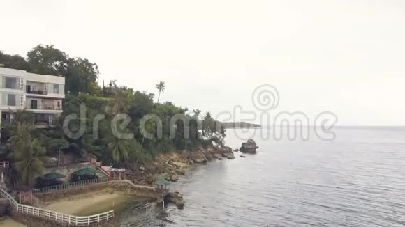 度假酒店在热带棕榈树之间的海岸鸟瞰无人驾驶飞机在多云的岛屿和海洋上观赏绿棕榈树视频的预览图