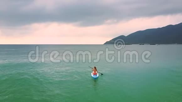 女孩坐在船上在天空下用桨在海洋中游泳视频的预览图