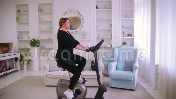 模特一个胖女人在家里骑着一辆固定的自行车视频的预览图