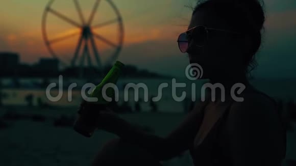 独自一个年轻的女人喝着瓶子里的啤酒在海滩上看日落快关门视频的预览图