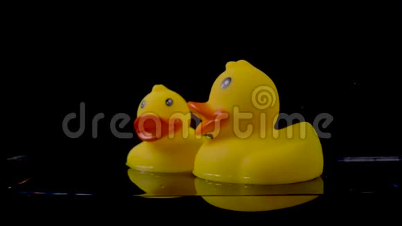 大大小小的橡胶鸭子漂浮在黑色背景的水面上视频的预览图