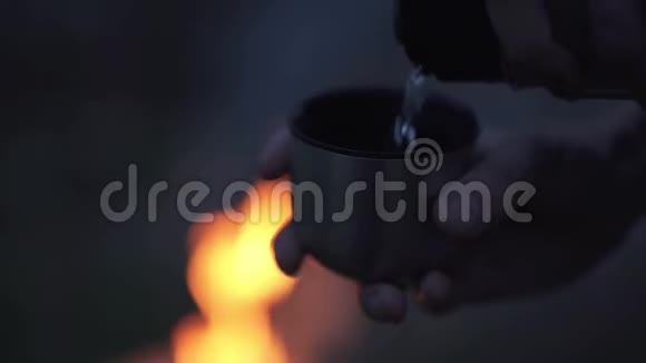 男人的手从热水瓶到杯水靠近火森林里的火堆旁视频的预览图