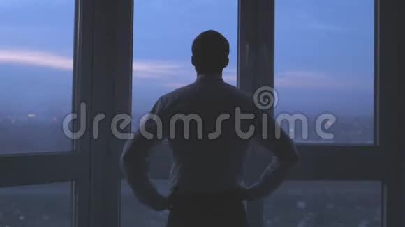 一个商人的背面站在窗户附近看着夜晚的城市背景3840x2160视频的预览图