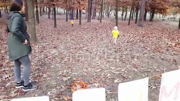 妈妈带着孩子在公园里收集秋天的树叶公园里有一个镶有秋天字样的白纸叶子花环视频的预览图