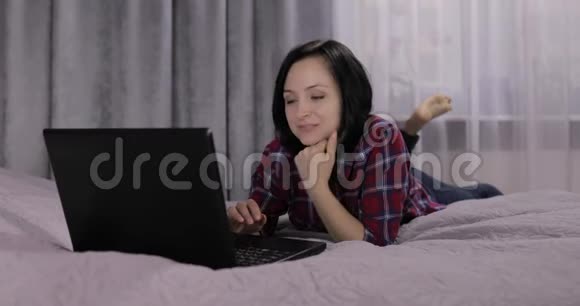 年轻女子躺在床上用笔记本电脑上的网络摄像头进行视频聊天视频的预览图