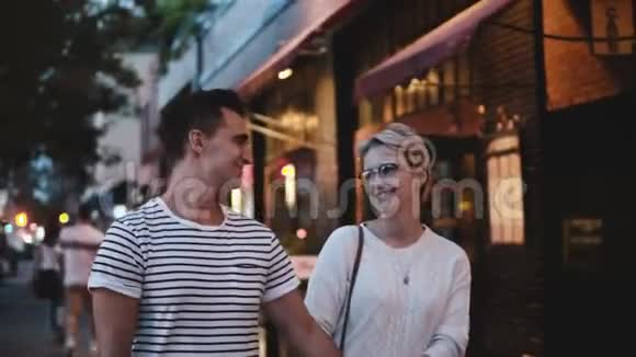 快乐微笑的西班牙男人和高加索女人牵着手说话微笑亲吻在纽约的黄昏街道上行走视频的预览图
