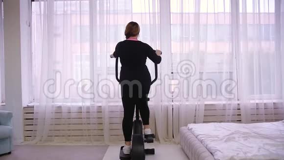 模特一个胖女人在家里骑着一辆固定的自行车视频的预览图